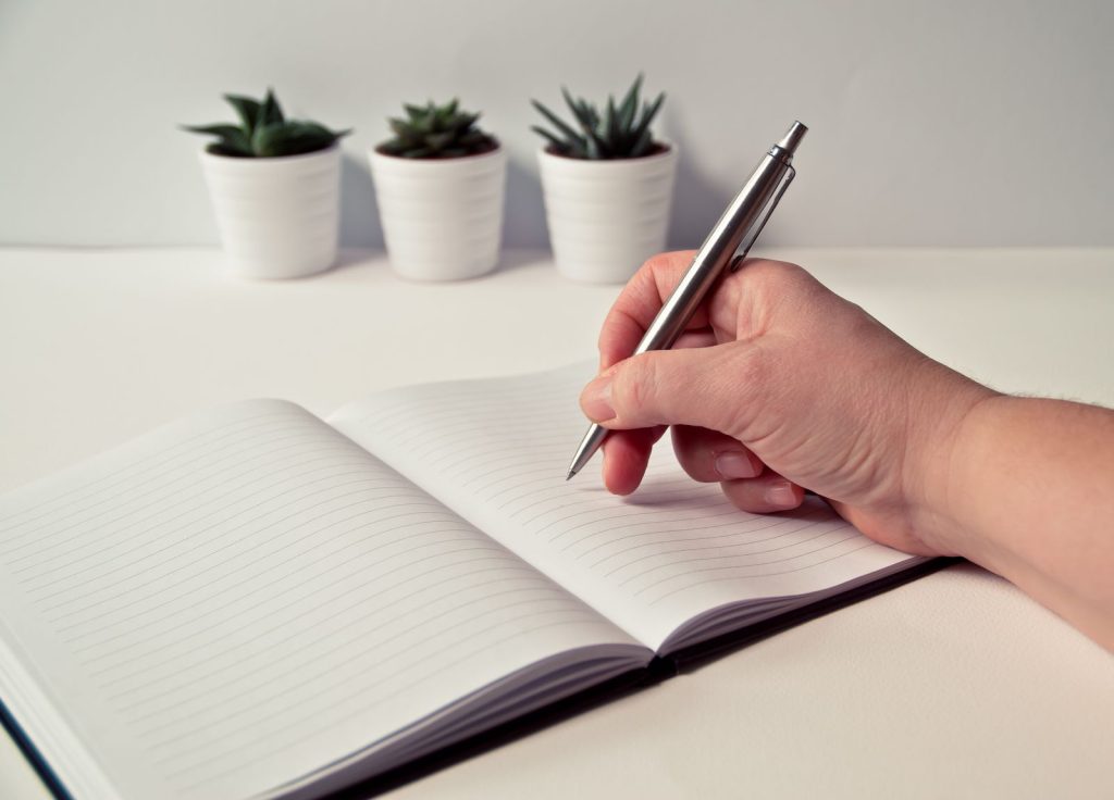 Persona escribiendo en una libreta junto a pequeñas plantas