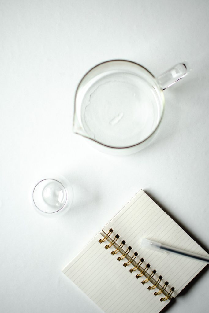 Jarra de cristal y libreta sobre una superficie blanca